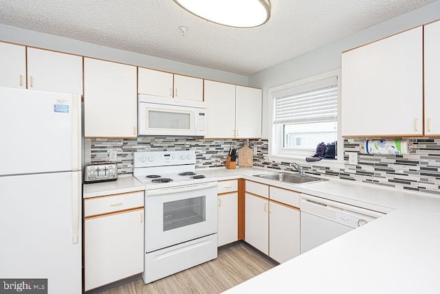 kitchen featuring light wood finished floors, light countertops, decorative backsplash, a sink, and white appliances