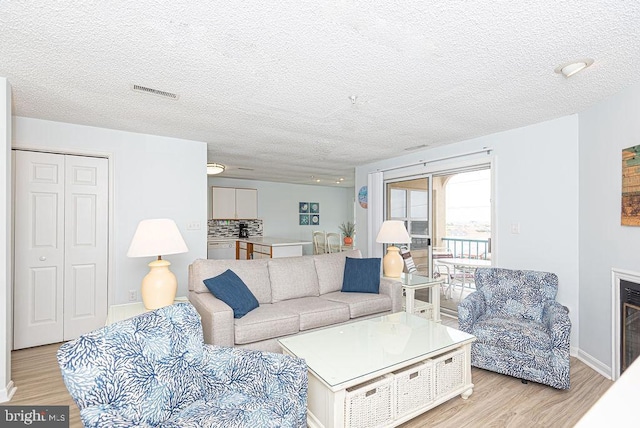 living room with light wood-style floors, visible vents, and a textured ceiling