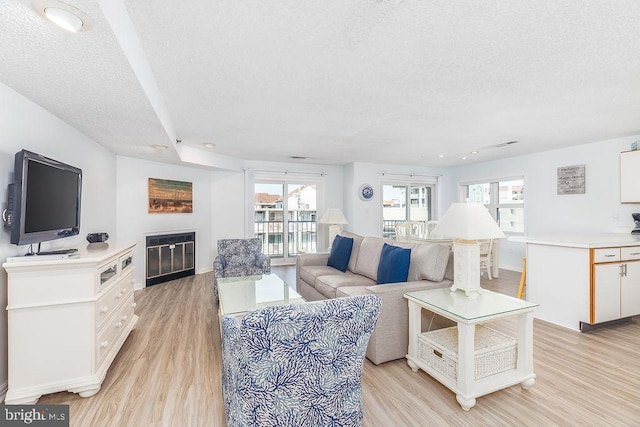 living area featuring light wood finished floors, a textured ceiling, and a glass covered fireplace