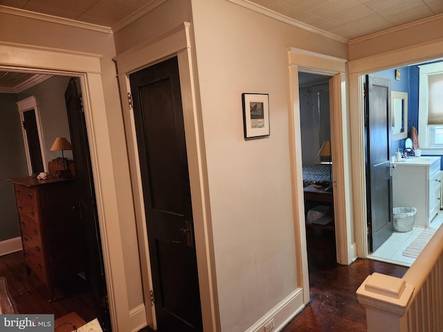 corridor featuring ornamental molding, a sink, dark wood finished floors, and baseboards