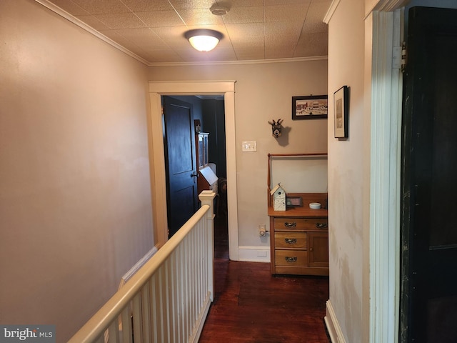 hall with dark wood-style floors, baseboards, an upstairs landing, and crown molding