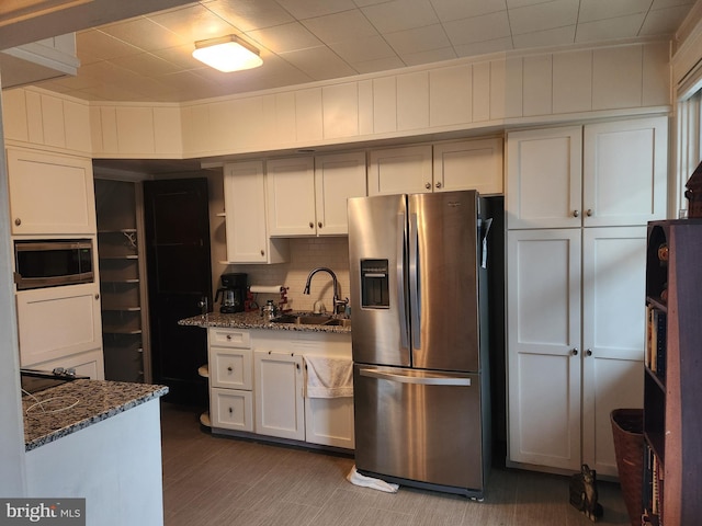 kitchen with white cabinetry, appliances with stainless steel finishes, dark stone counters, and a sink