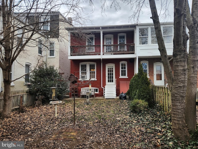 view of front facade with brick siding, a chimney, entry steps, fence, and a balcony