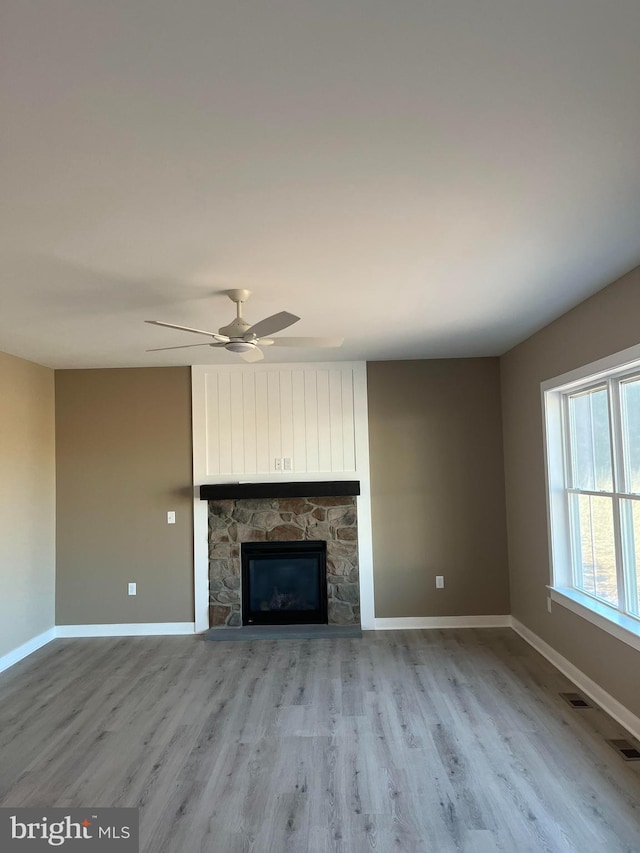 unfurnished living room featuring a stone fireplace, light wood-type flooring, and baseboards