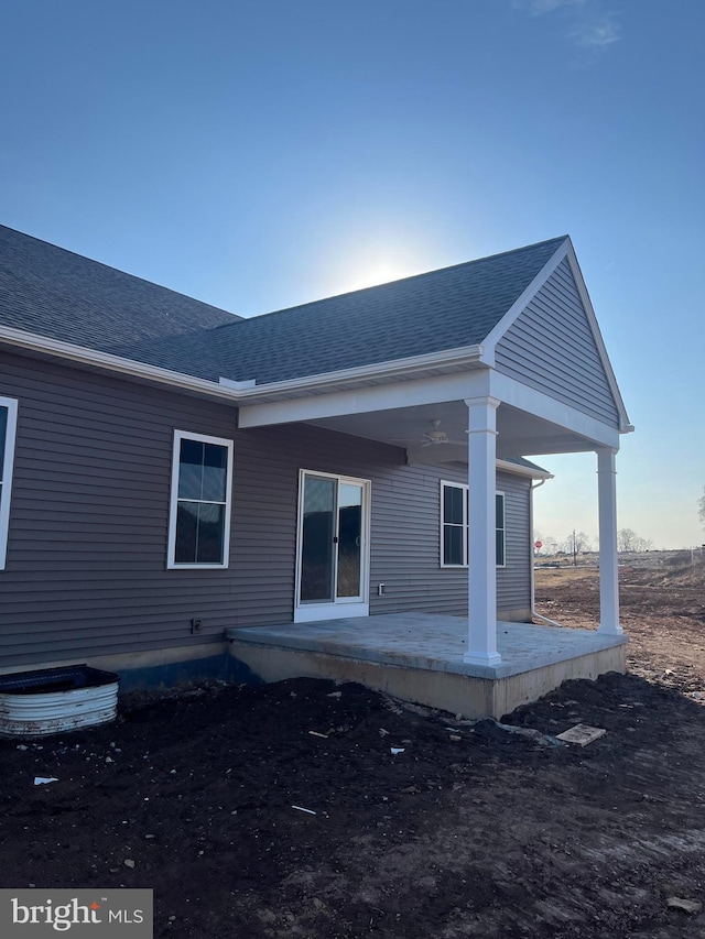 back of property with roof with shingles and a patio