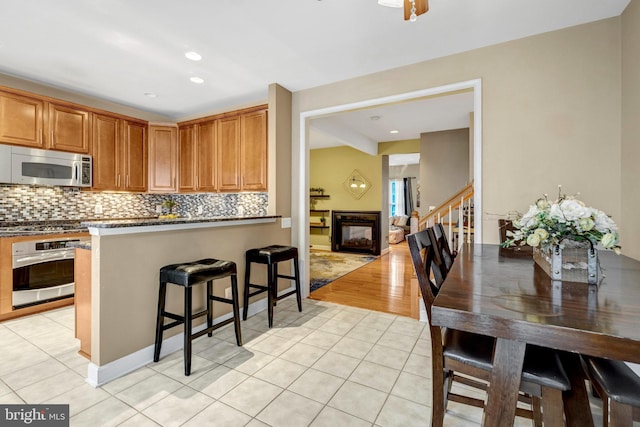 kitchen featuring tasteful backsplash, light tile patterned floors, a multi sided fireplace, and stainless steel appliances