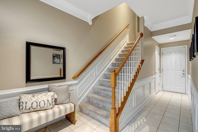 staircase featuring visible vents, a decorative wall, wainscoting, tile patterned flooring, and crown molding