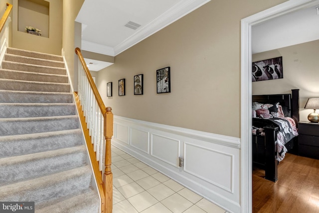 stairs with visible vents, a wainscoted wall, crown molding, and a decorative wall