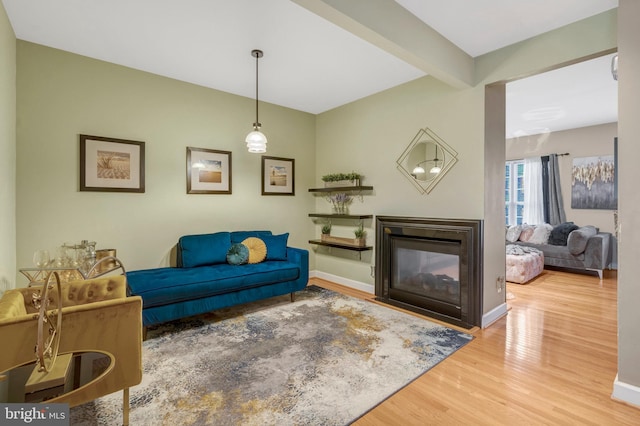 living room with beamed ceiling, a multi sided fireplace, baseboards, and wood finished floors