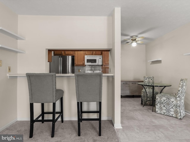 kitchen with white microwave, a peninsula, tasteful backsplash, and freestanding refrigerator