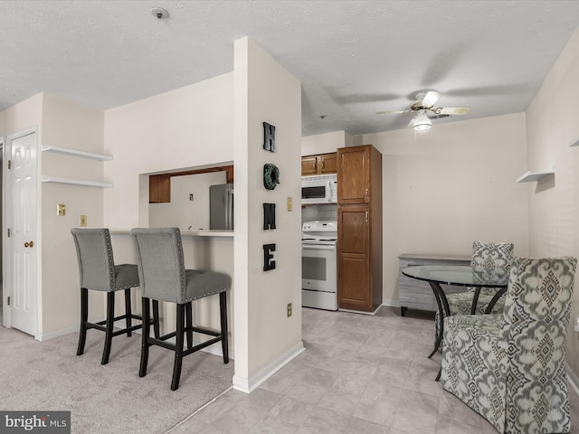 kitchen with brown cabinets, a kitchen breakfast bar, white appliances, a textured ceiling, and a ceiling fan