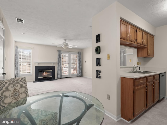 kitchen featuring visible vents, dishwasher, light carpet, brown cabinets, and a sink