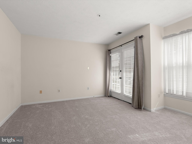 carpeted empty room with a healthy amount of sunlight, visible vents, and baseboards