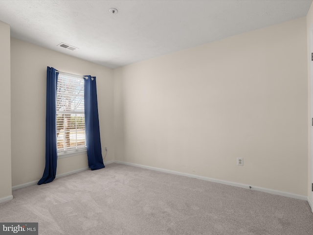 spare room featuring light colored carpet, visible vents, and baseboards