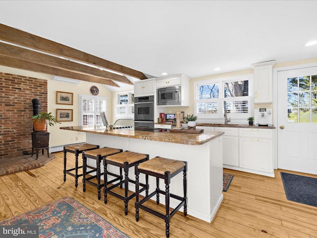 kitchen featuring stainless steel appliances, light wood finished floors, plenty of natural light, a kitchen bar, and a wood stove