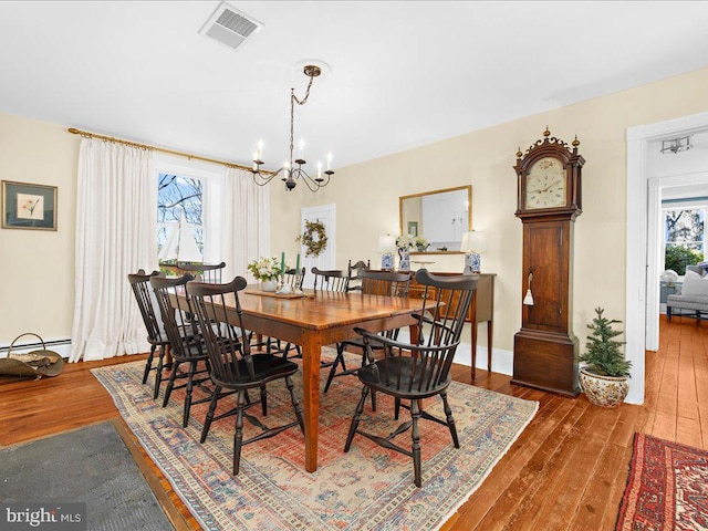 dining space with baseboards, visible vents, hardwood / wood-style floors, and an inviting chandelier