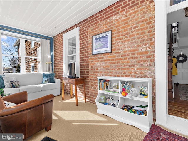 carpeted living room featuring brick wall