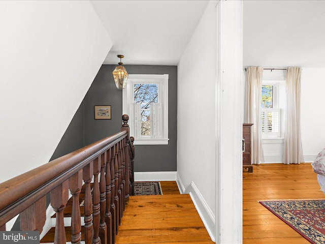 hall with an upstairs landing, baseboards, plenty of natural light, and hardwood / wood-style floors