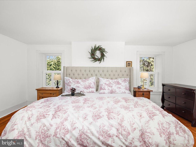 bedroom with multiple windows, wood finished floors, and baseboards