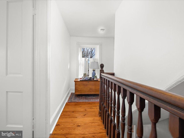 hallway featuring wood finished floors, an upstairs landing, and baseboards