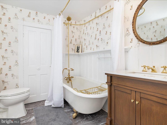 bathroom featuring a freestanding bath, toilet, wainscoting, vanity, and wallpapered walls