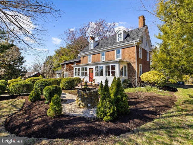 back of property featuring a sunroom, an outdoor fire pit, a chimney, and brick siding