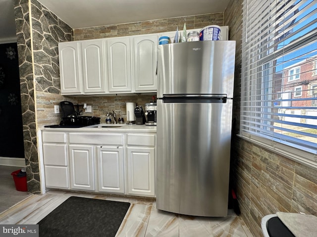 kitchen featuring light countertops, a sink, freestanding refrigerator, and white cabinets