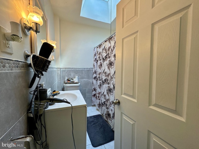 bathroom with toilet, a wainscoted wall, tile patterned floors, vanity, and tile walls