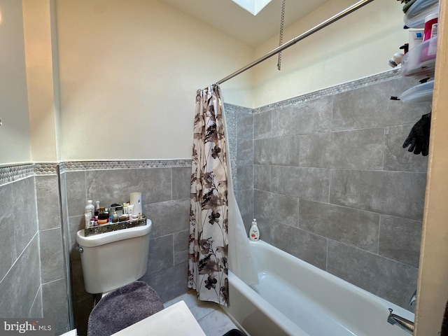 full bathroom with toilet, a skylight, tile walls, wainscoting, and shower / bath combination with curtain