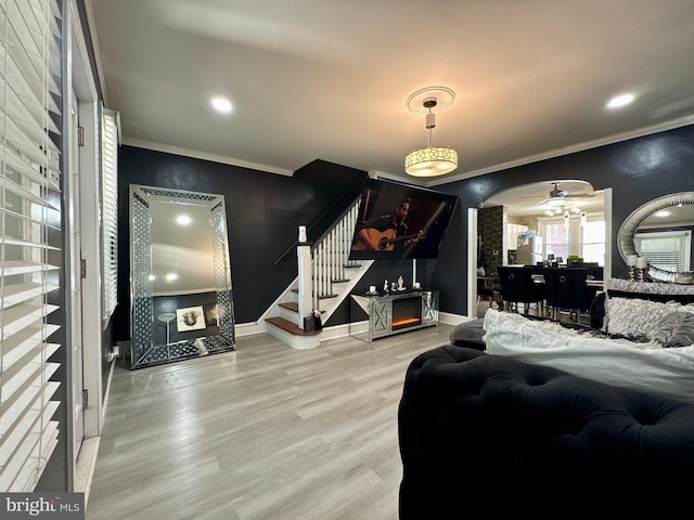 living room featuring arched walkways, wood finished floors, baseboards, stairway, and crown molding