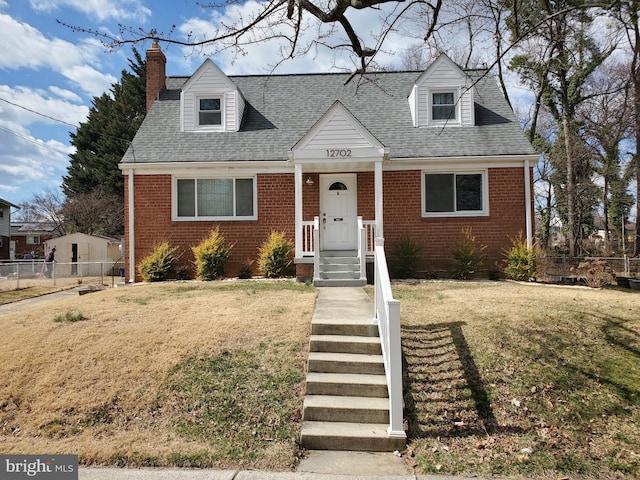 cape cod-style house featuring brick siding, a chimney, a front yard, and fence