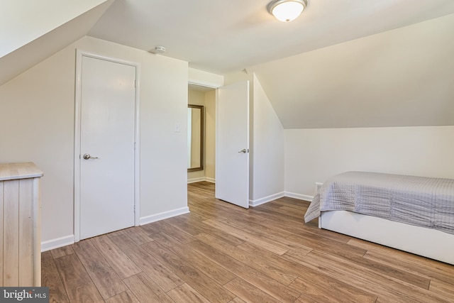 unfurnished bedroom featuring baseboards, wood finished floors, and vaulted ceiling