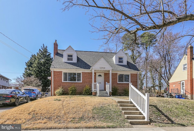 cape cod house with brick siding, a chimney, and roof with shingles