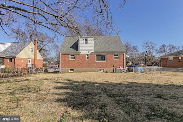 rear view of house with a yard, central air condition unit, brick siding, and a fenced backyard