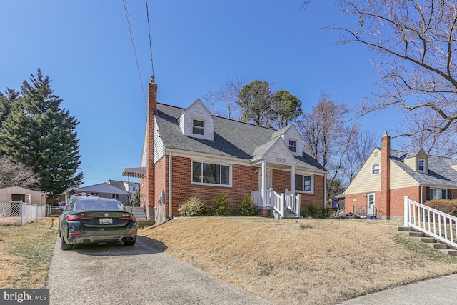 cape cod house featuring brick siding, roof with shingles, a chimney, and fence