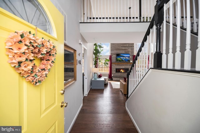 entryway featuring a large fireplace, wood finished floors, a towering ceiling, baseboards, and stairs