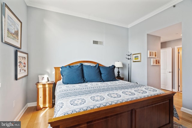 bedroom featuring ornamental molding, light wood-type flooring, visible vents, and baseboards