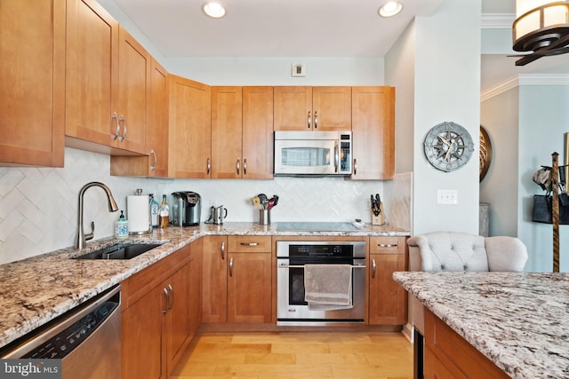 kitchen featuring light wood finished floors, tasteful backsplash, appliances with stainless steel finishes, a sink, and light stone countertops