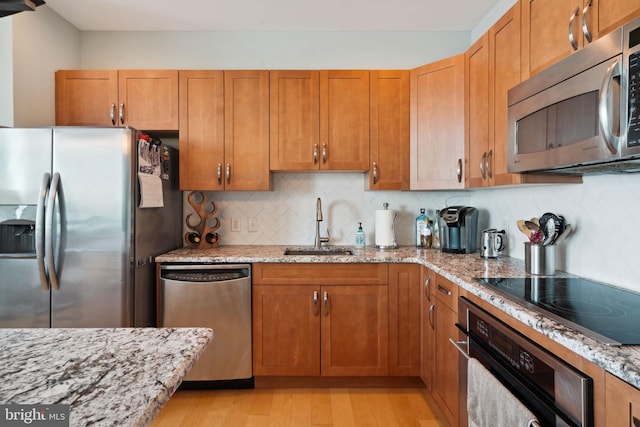 kitchen featuring light wood finished floors, appliances with stainless steel finishes, a sink, and light stone countertops