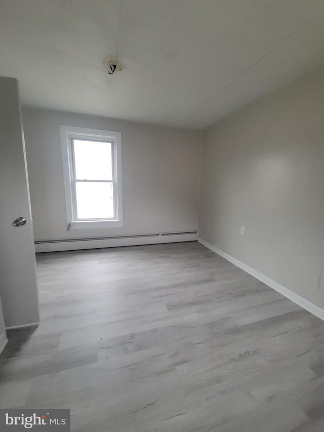 unfurnished room featuring a baseboard heating unit, baseboards, and wood finished floors