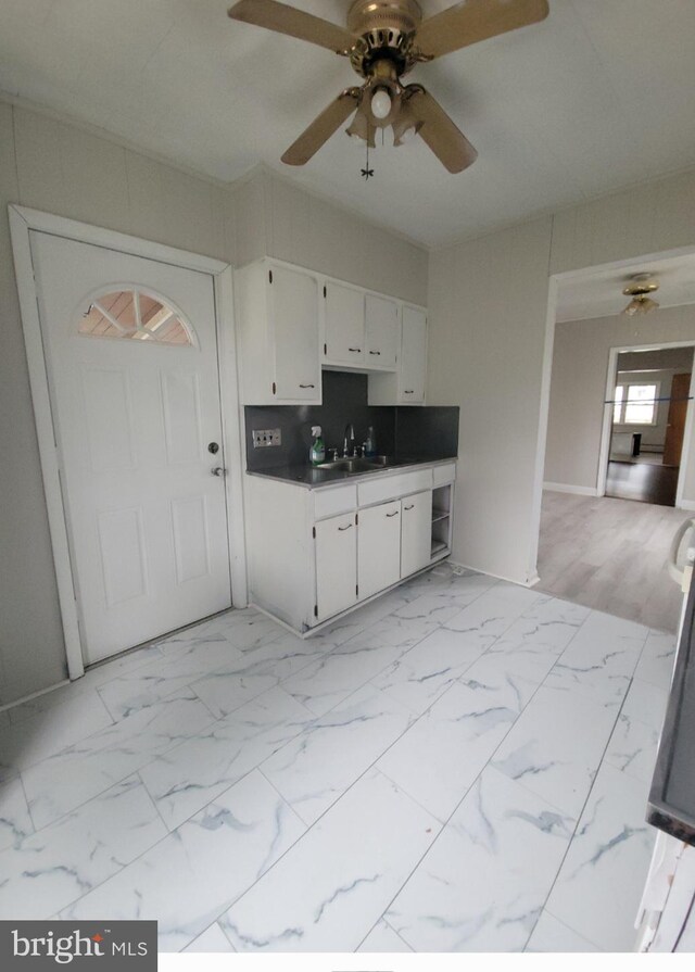kitchen with ceiling fan, white cabinets, marble finish floor, a sink, and dark countertops