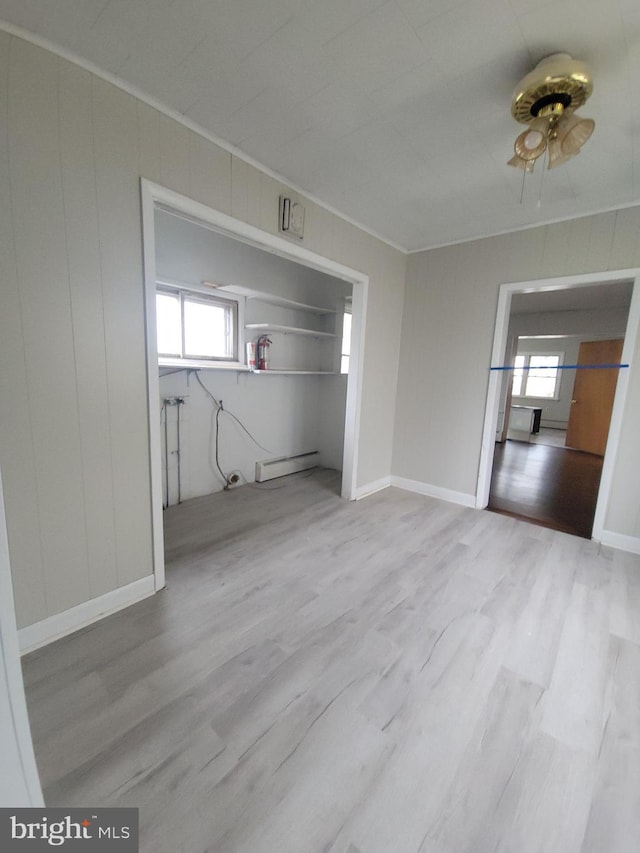 unfurnished bedroom featuring wood finished floors, a baseboard heating unit, and multiple windows