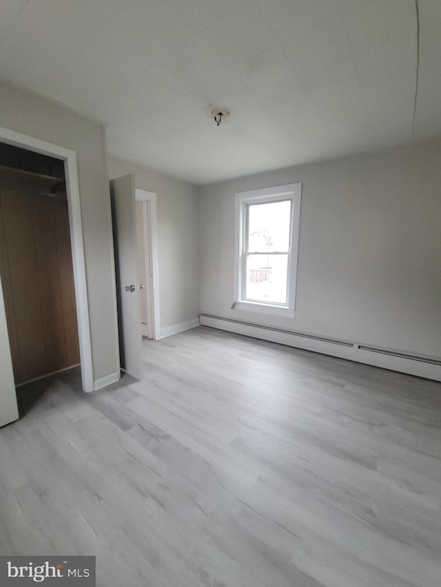 unfurnished bedroom with baseboards, a baseboard heating unit, and wood finished floors