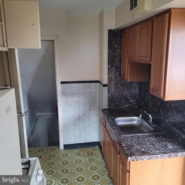 kitchen featuring visible vents, brown cabinets, a sink, and range with gas stovetop