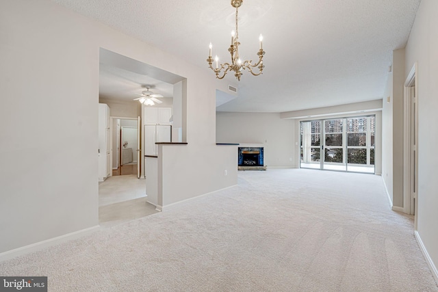 unfurnished living room with a textured ceiling, ceiling fan with notable chandelier, carpet floors, a fireplace, and baseboards