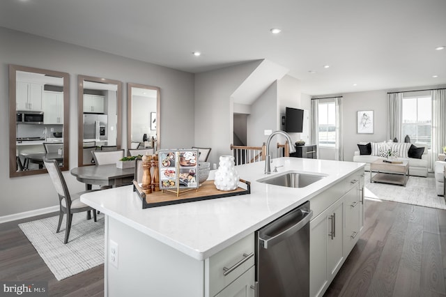 kitchen with a sink, open floor plan, appliances with stainless steel finishes, dark wood-style floors, and a center island with sink