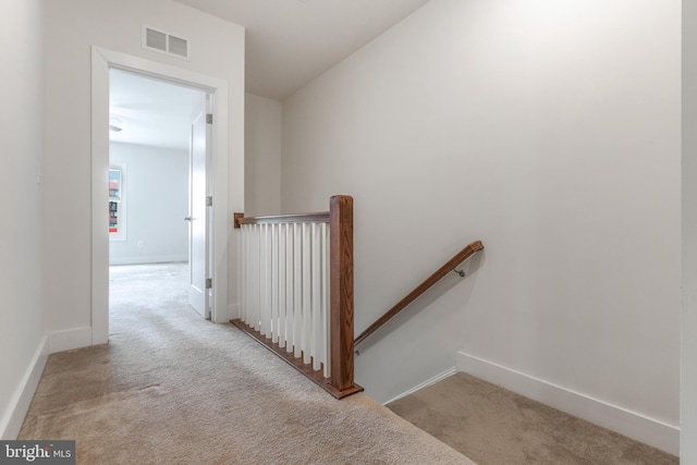 hall featuring an upstairs landing, visible vents, carpet floors, and baseboards