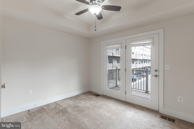 carpeted spare room featuring a raised ceiling, baseboards, visible vents, and ceiling fan