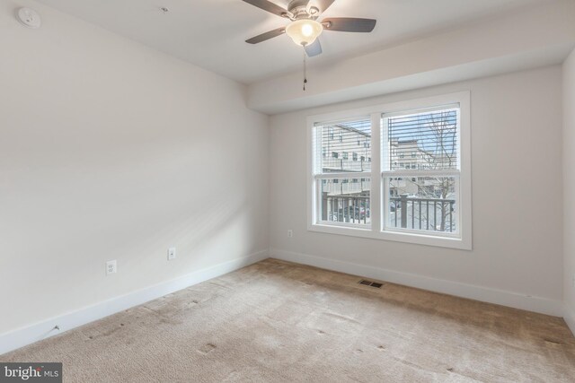 carpeted spare room featuring a ceiling fan, visible vents, and baseboards