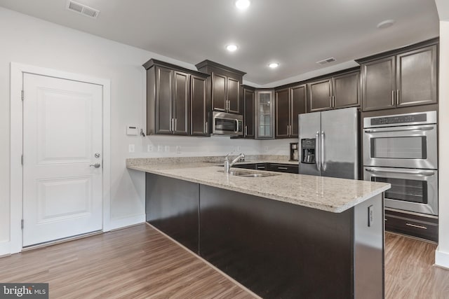 kitchen with visible vents, glass insert cabinets, appliances with stainless steel finishes, light wood-style floors, and a sink